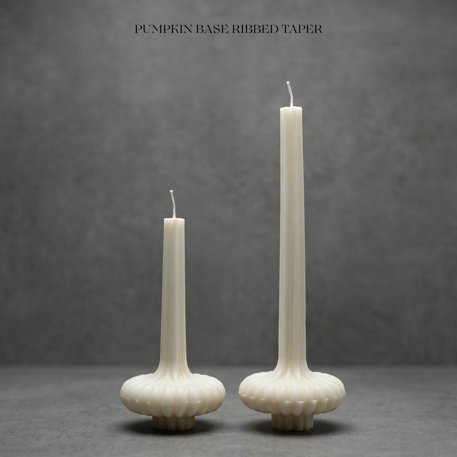 Two ribbed taper candles on pumpkin bases against a gray background