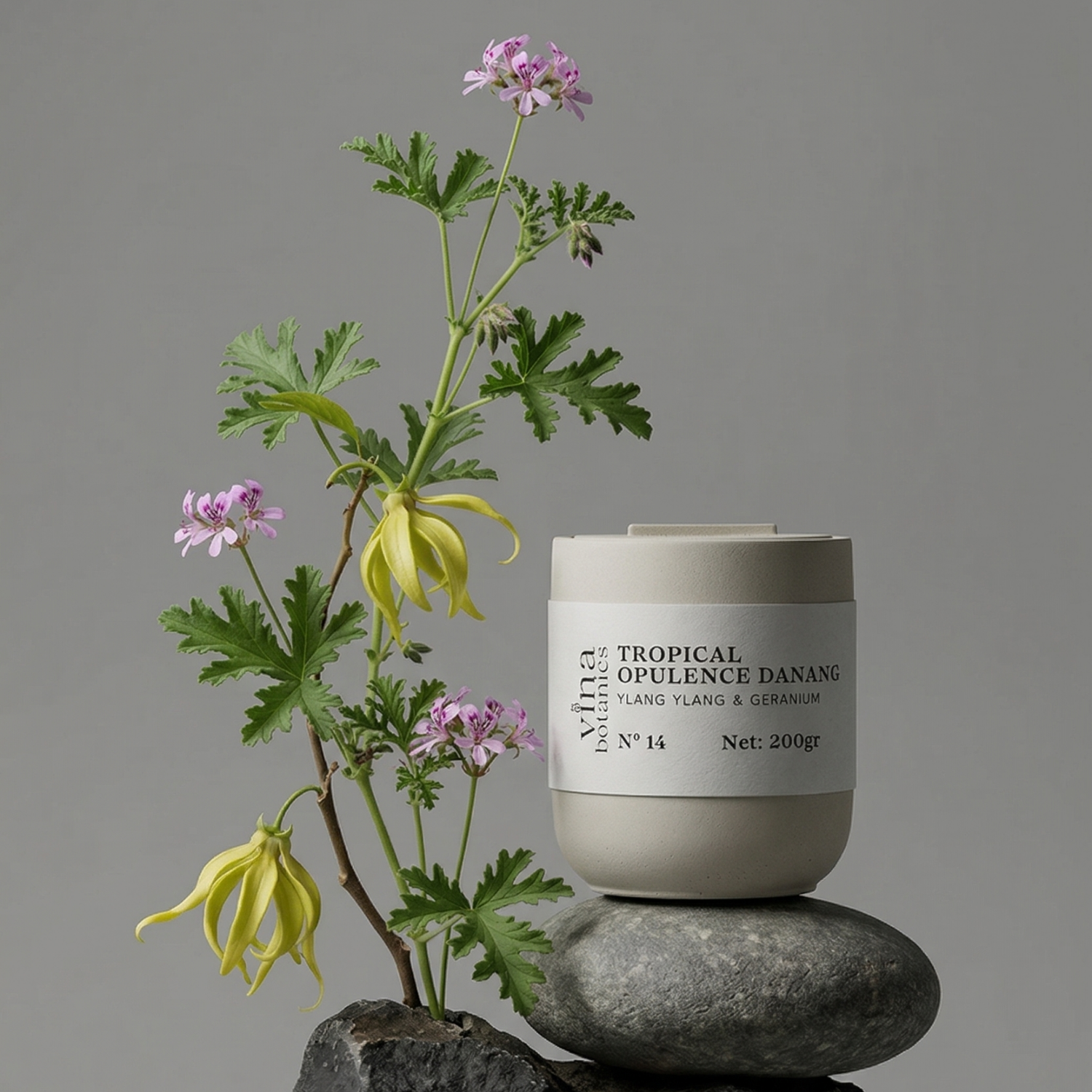 Candle labeled 'Tropical Opulence Danang' on a rock with a plant against a gray background