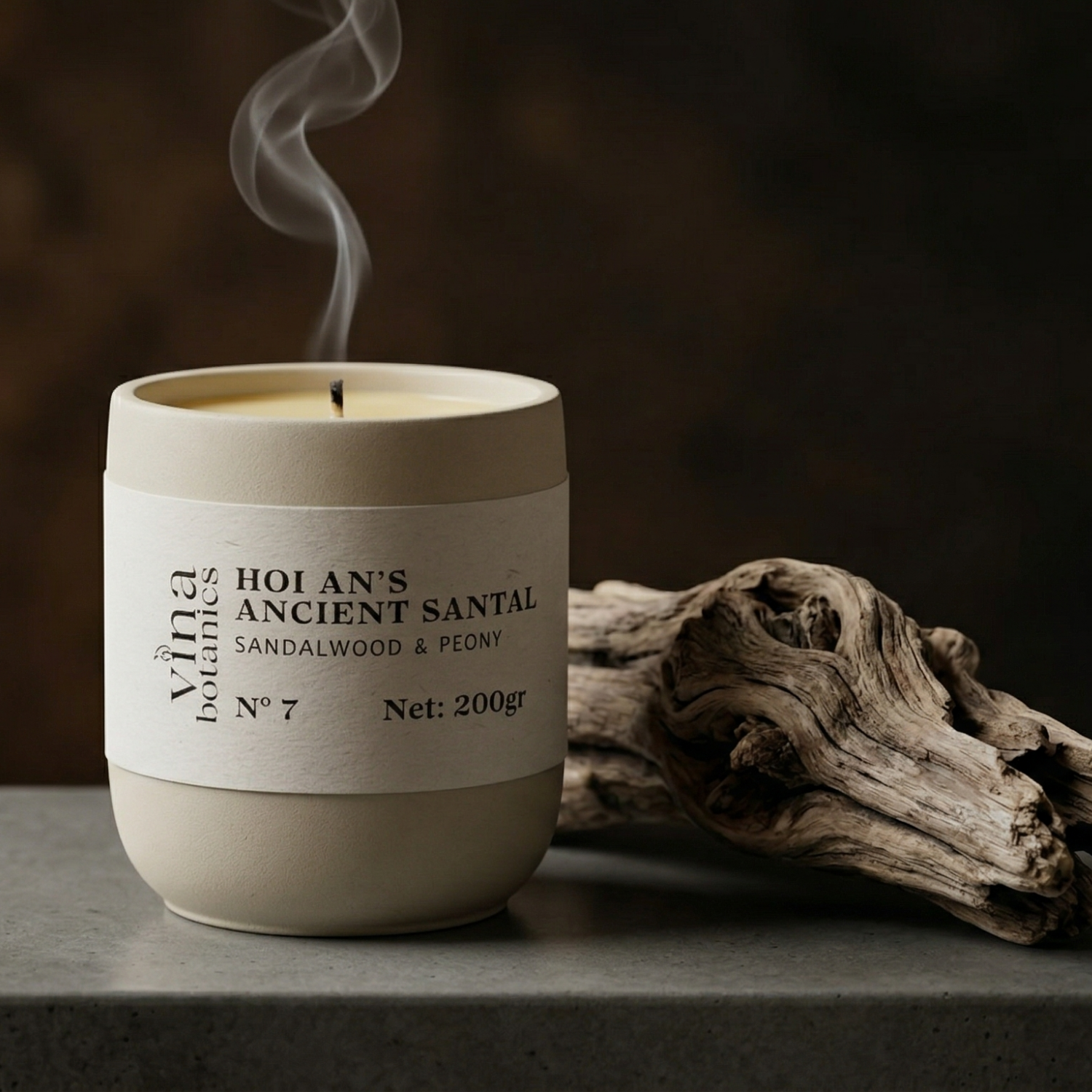 Candle with a label on a dark surface next to a piece of driftwood