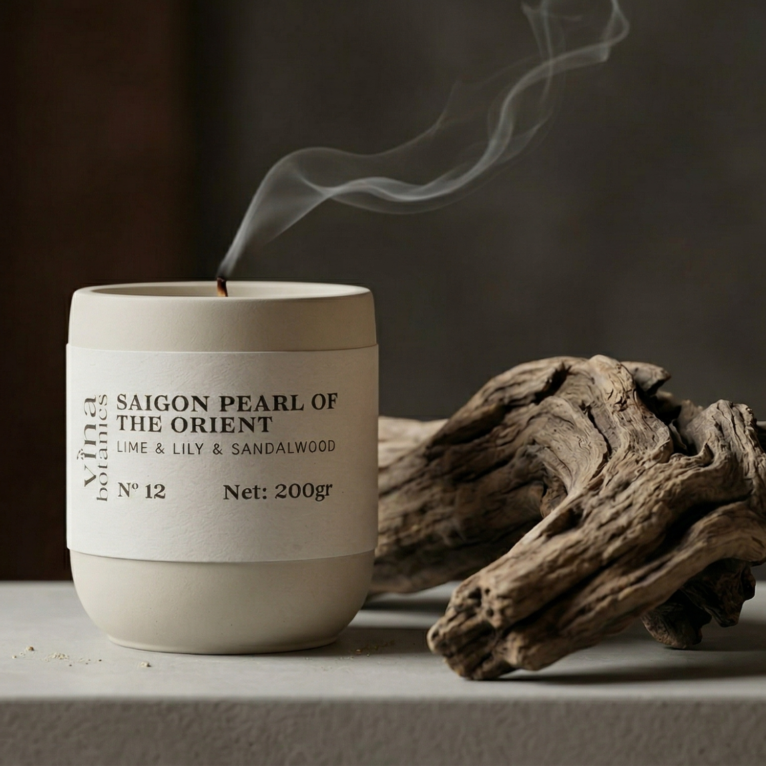 Ceramic candle with 'Saigon Pearl of the Orient' label and smoking candle next to wooden driftwood on a dark background