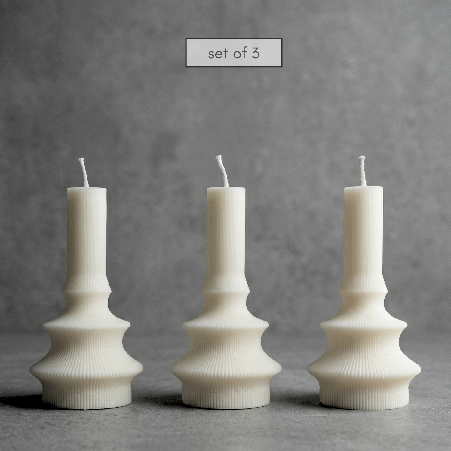 Set of three white textured candles on a gray background