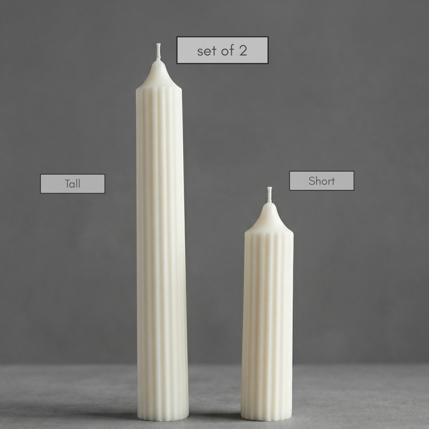 Two ribbed candles, one tall and one short, on a gray surface with a dark gray background.