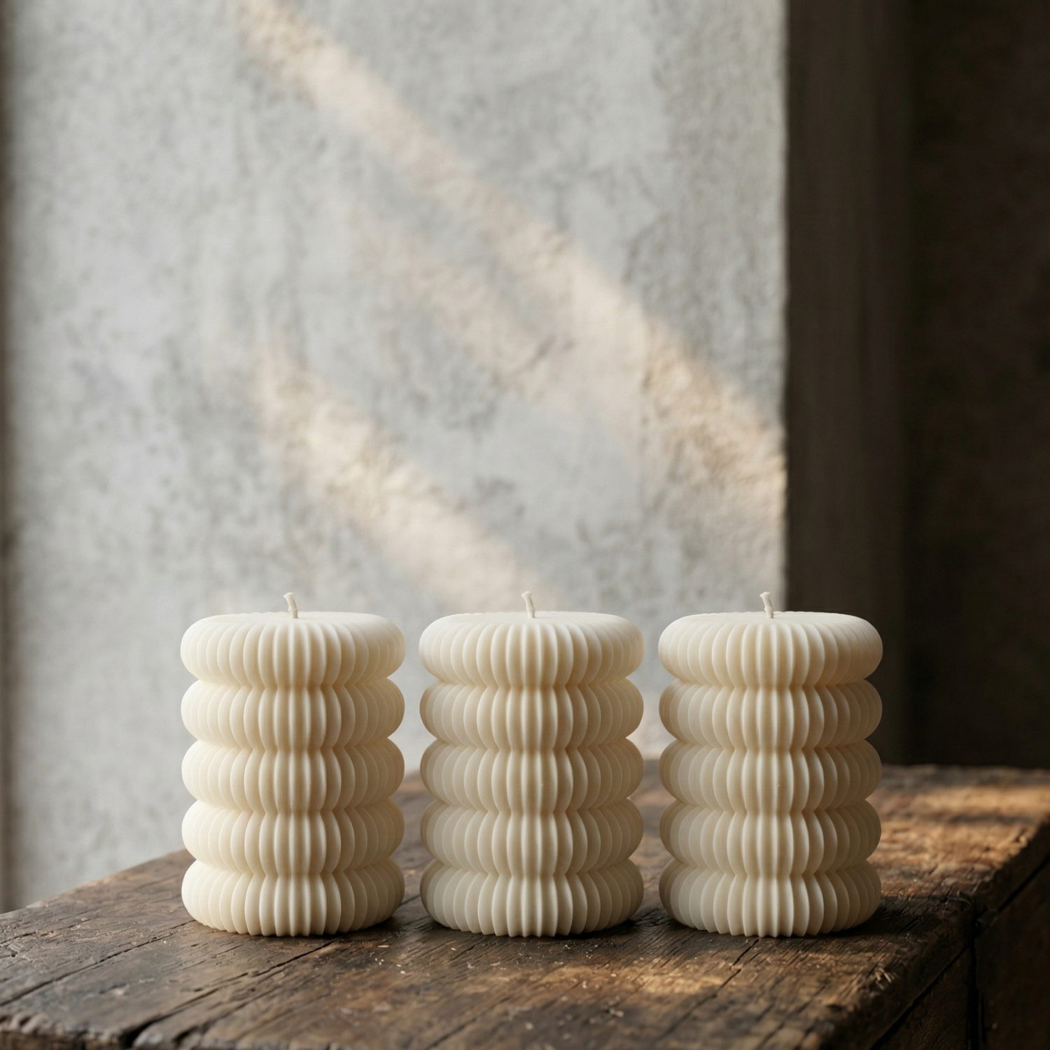 Three ribbed candle holders on a wooden surface with a textured wall background