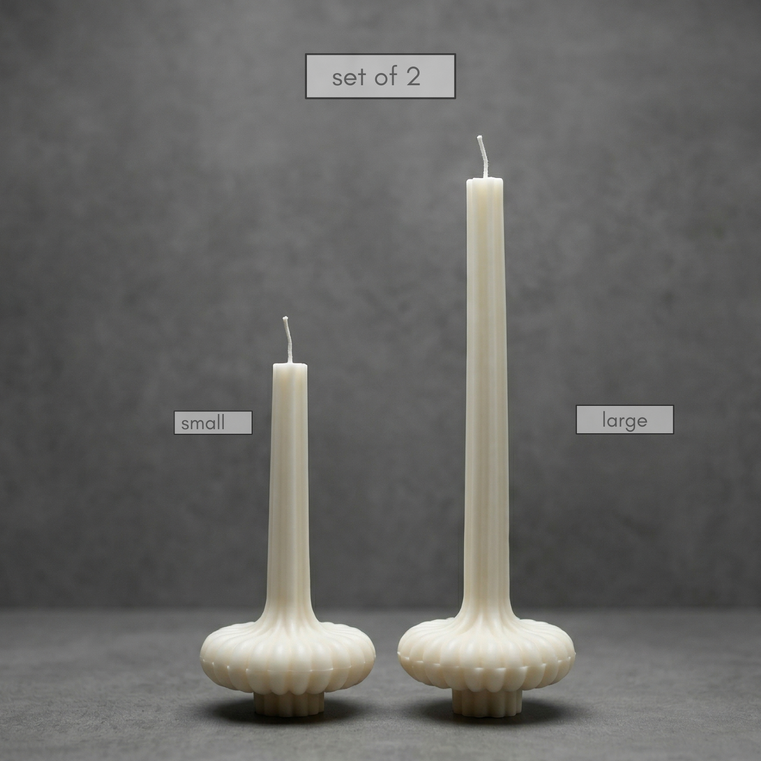 Two candle holders with candles, one small and one large, on a gray background.