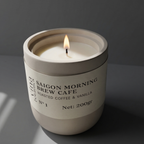 Candle in a white container labeled 'Saigon Morning Brew Cafe' on a dark background