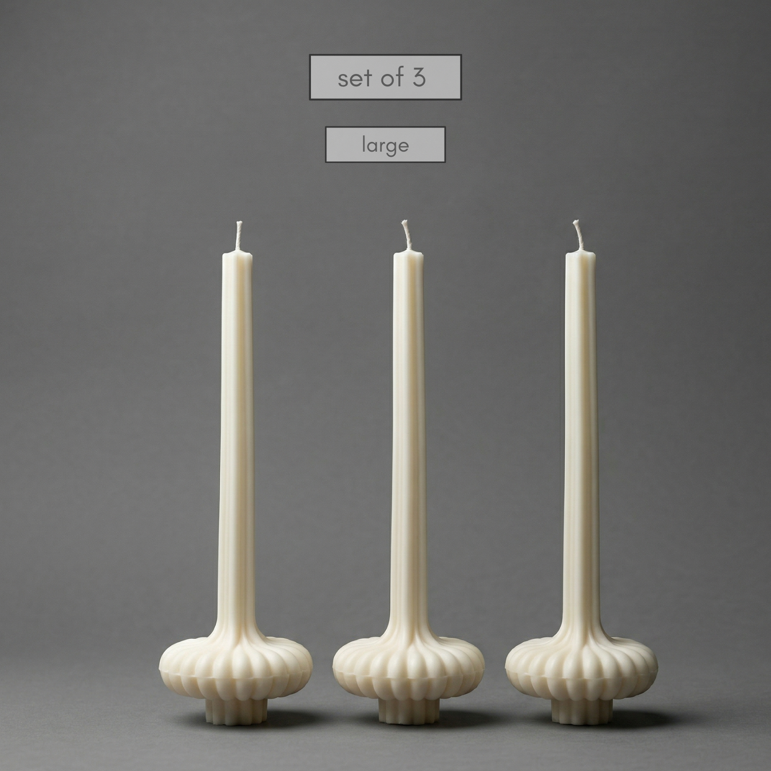 Set of three large white candles with textured holders on a gray background
