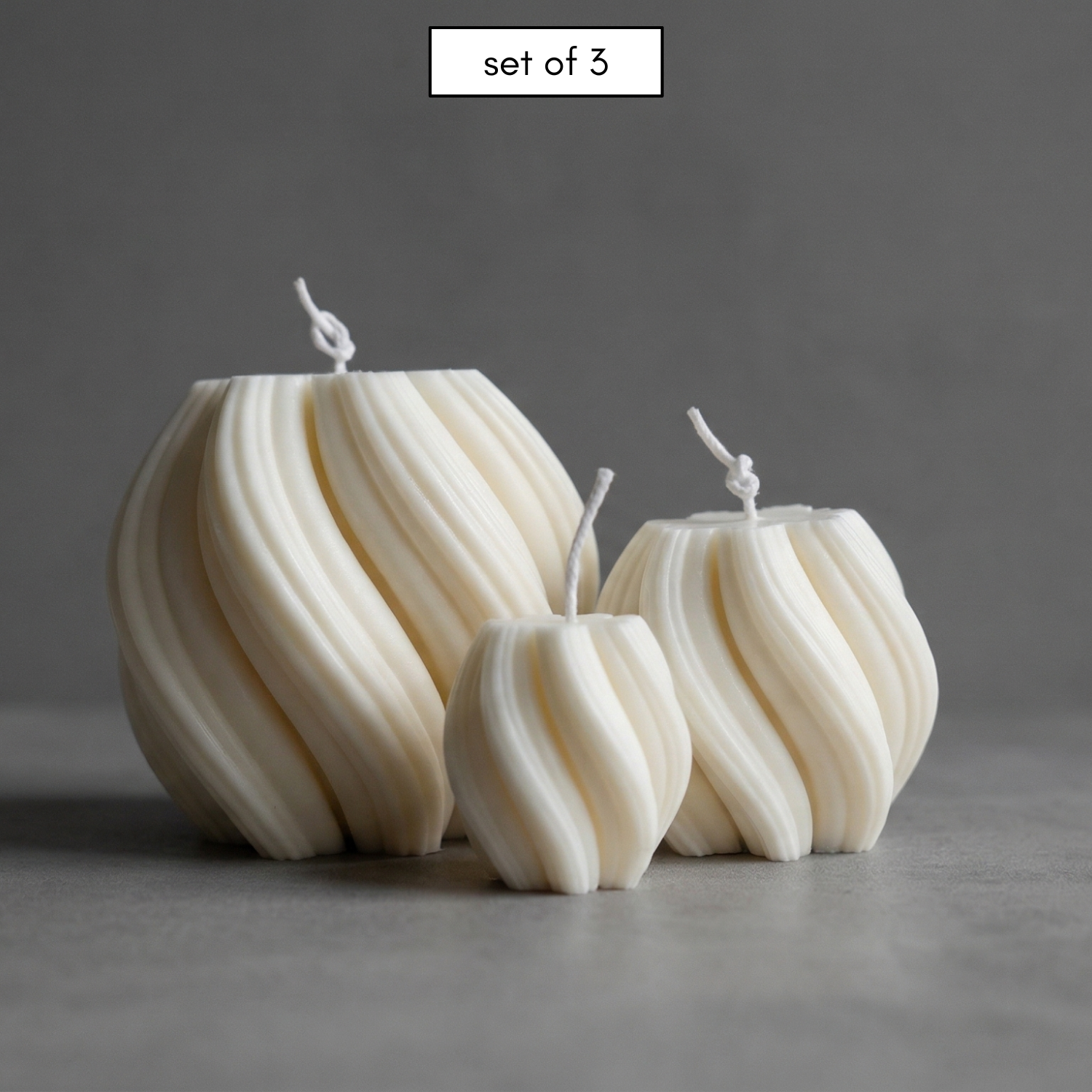 Set of three white textured candles on a gray background